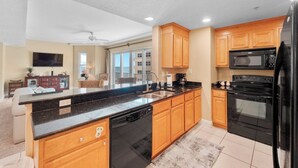A modern kitchen with wooden cabinets, a black countertop, a built-in dishwasher, a microwave, a stove, and a refrigerator.