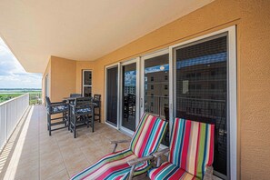 Un balcon avec une table et des chaises, un canapé à rayures et une porte-fenêtre coulissante donnant sur un espace piscine.
