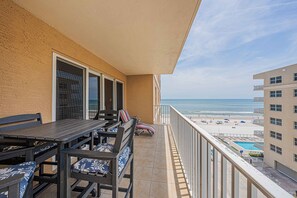 Un balcón con mesa y sillas, con vista a una playa que tiene piscina y sombrillas.