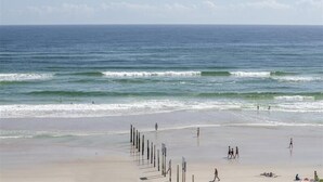 A beach with waves, people walking, and a row of poles.