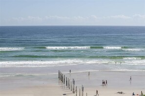 A beach with waves, people walking, and a row of poles.