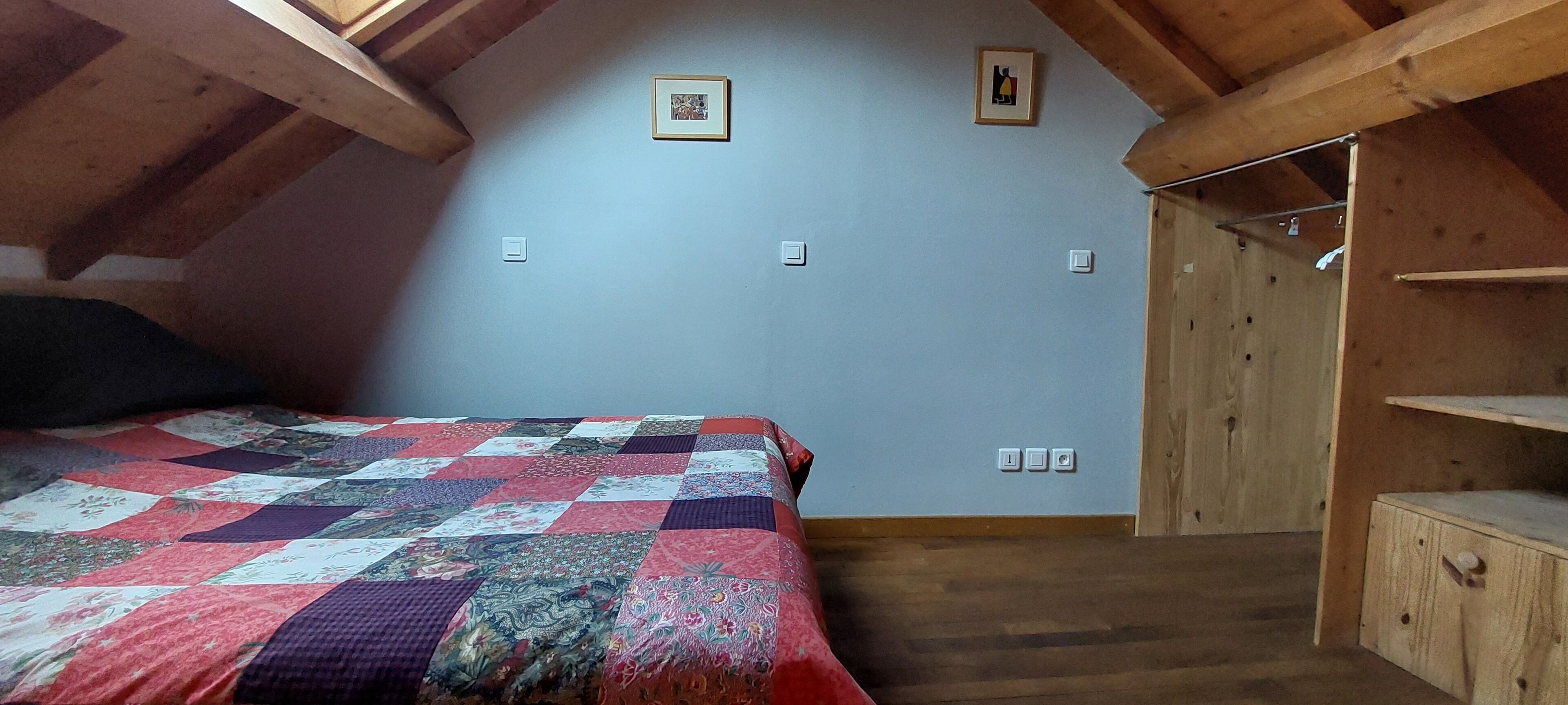 A bedroom with a wooden ceiling, a quilted bedspread, and a wooden wardrobe.