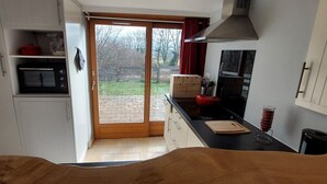 Eine Küche mit einer Glastür zum Garten, einer Mikrowelle, einem roten Wasserkocher und einem Schneidebrett auf der Arbeitsplatte.