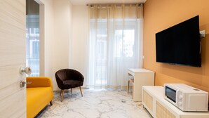 Ein modernes Zimmer mit einem gelben Sofa, einem dunklen Sessel, einem kleinen Schreibtisch, einem Fernseher und einer Mikrowelle.