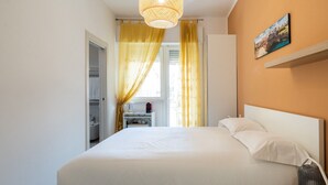 Habitación de hotel con cama, mesita de noche, lámpara, un cuadro en la pared y ventana con cortinas.