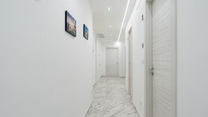 Un pasillo con paredes blancas, suelo de mármol y puertas que dan a habitaciones. Hay dos cuadros en la pared.