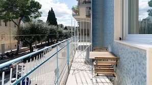 Un balcon donnant sur une rue, un mur recouvert de carreaux et un banc en bois.