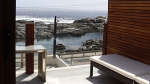 Un balcón con vista al océano, un separador de madera y un espacio para sentarse.