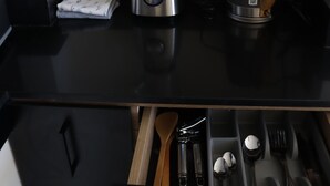 Una cocina con encimera negra, una licuadora, un hervidor y un cajón con utensilios.
