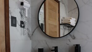 Un baño con tocador de madera, un lavabo negro, un espejo y un secador de pelo montado en la pared.