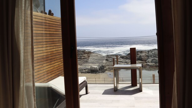 Habitación con vista al océano a través de una ventana, pared de madera y una pequeña mesa.