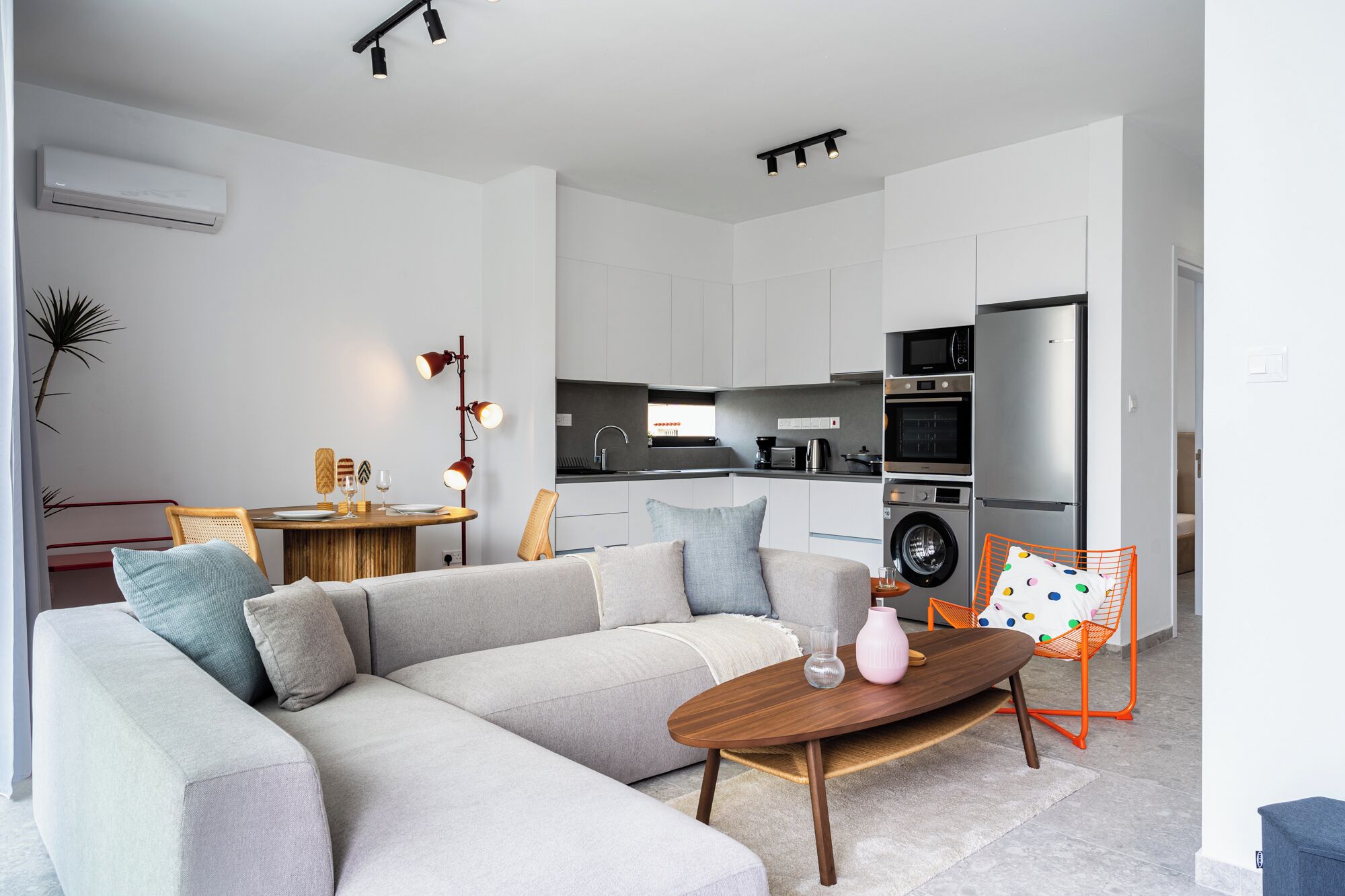 Una sala moderna con un sofá modular, una mesa de centro de madera y una cocina con electrodomésticos.