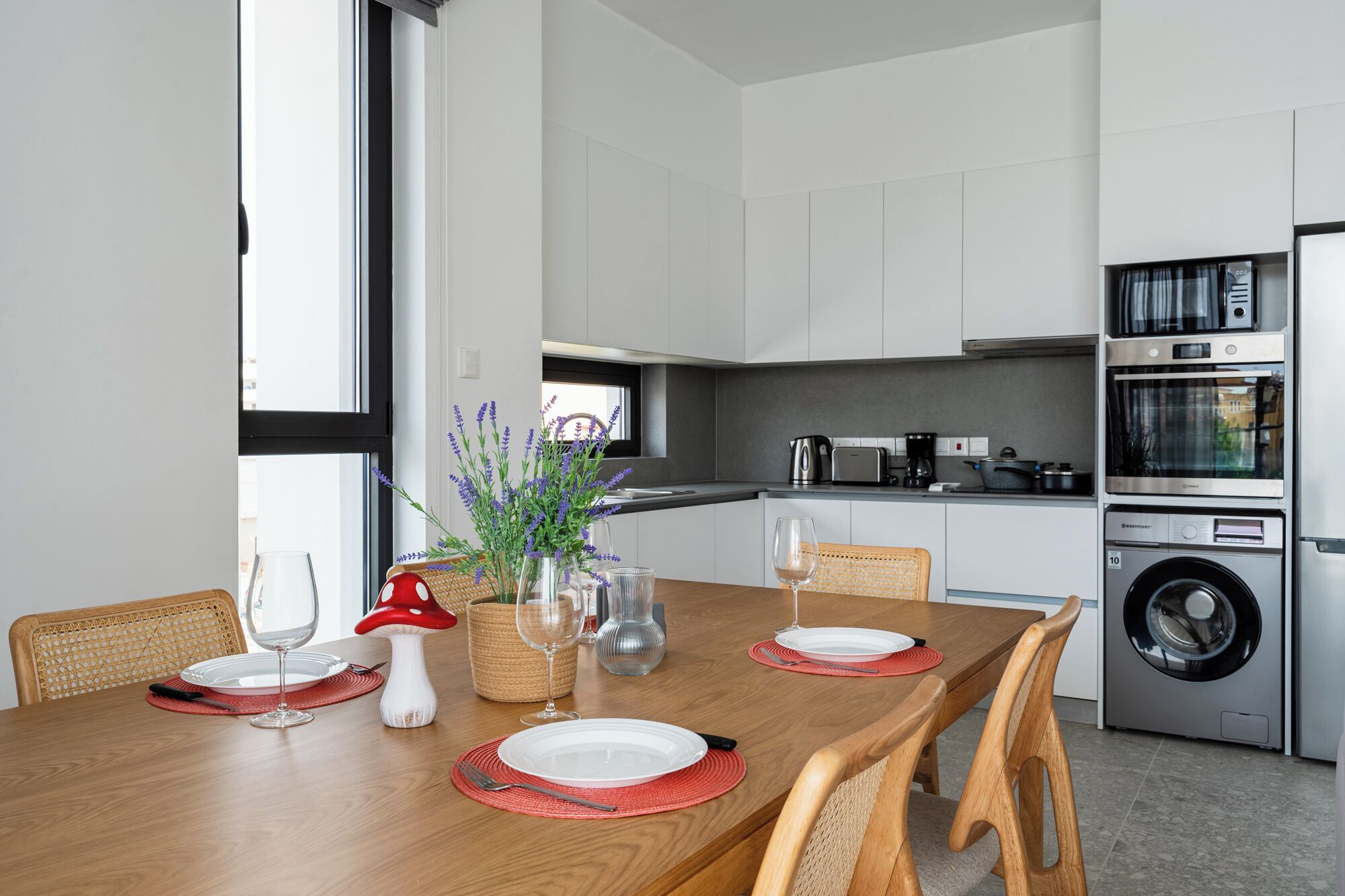 A modern kitchen with white cabinets, a dining table set with plates, glasses, and a decorative mushroom centerpiece.