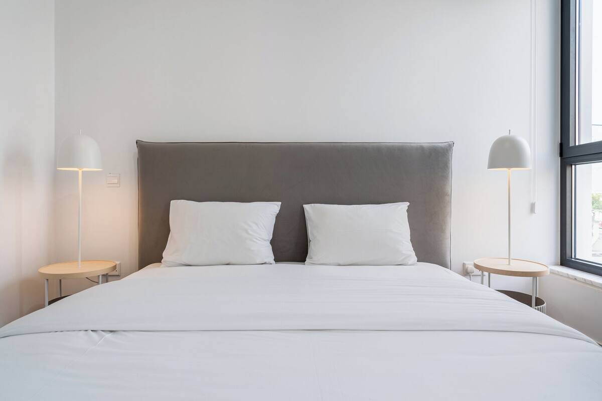 A modern bedroom with a large bed, two bedside tables, and a window.