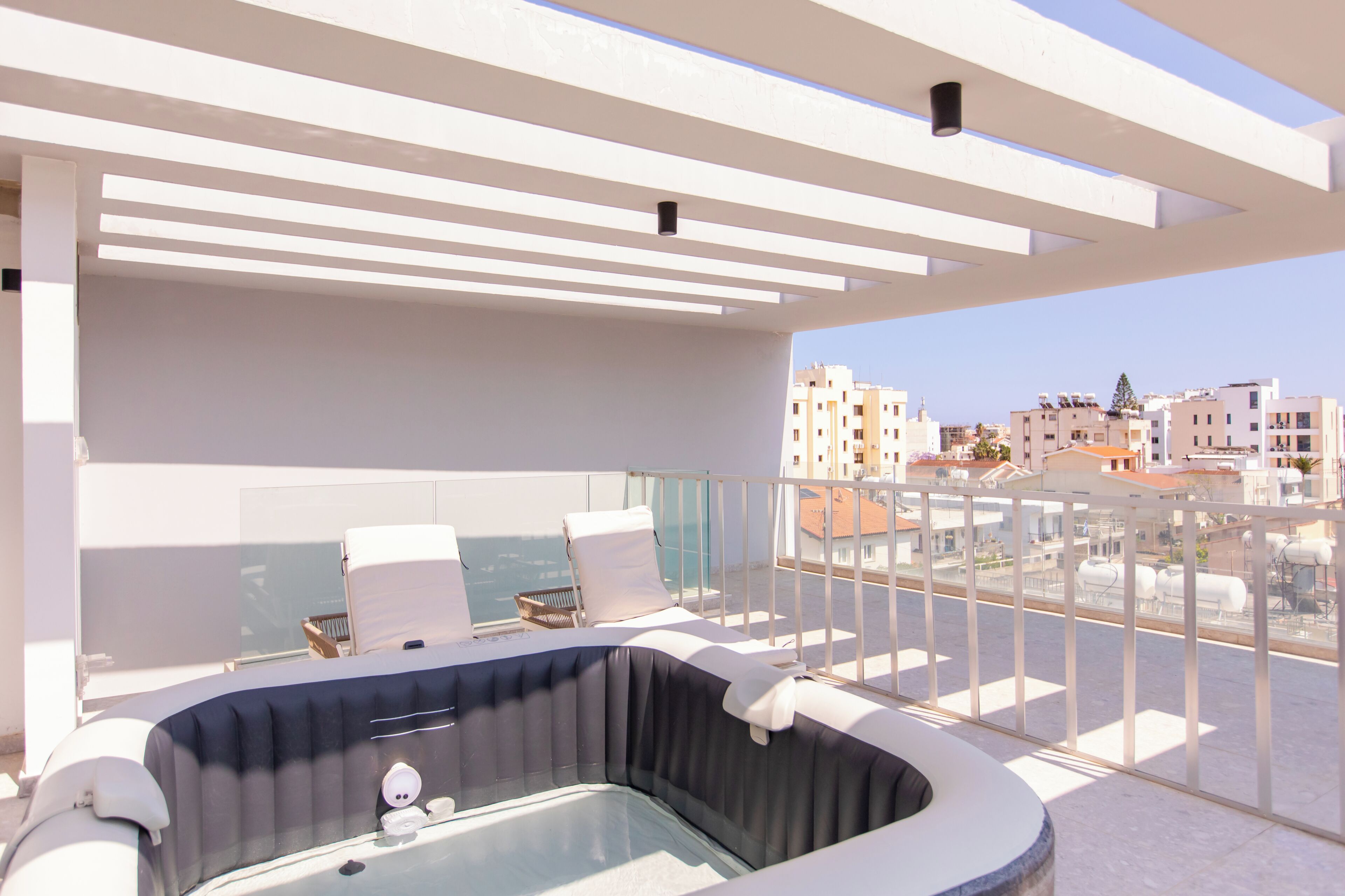 Terraço no topo do prédio com banheira de hidromassagem, espreguiçadeiras e vista para a paisagem urbana.