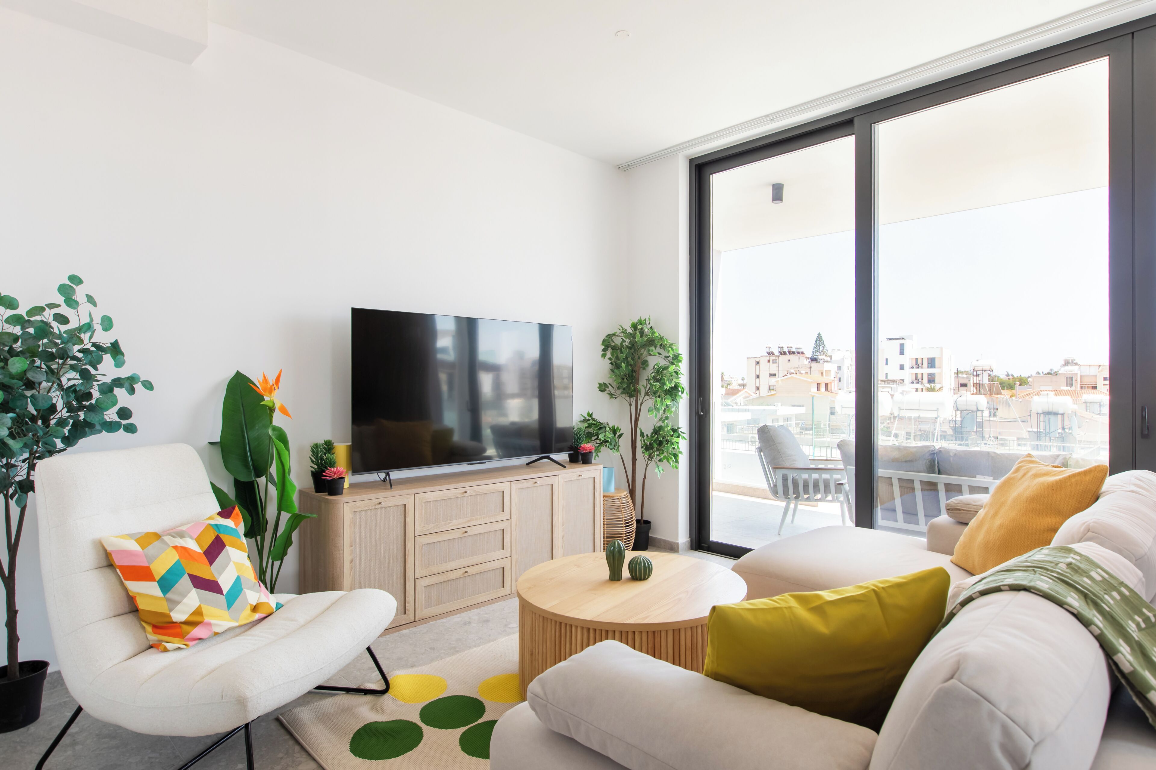 A modern living room with a flat-screen TV, a sofa, a chair, and a dining table.