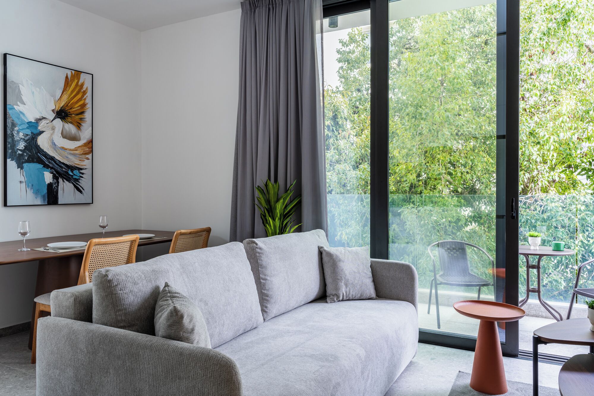 A modern living room with a grey sofa, a dining table with chairs, and a balcony with a glass railing.