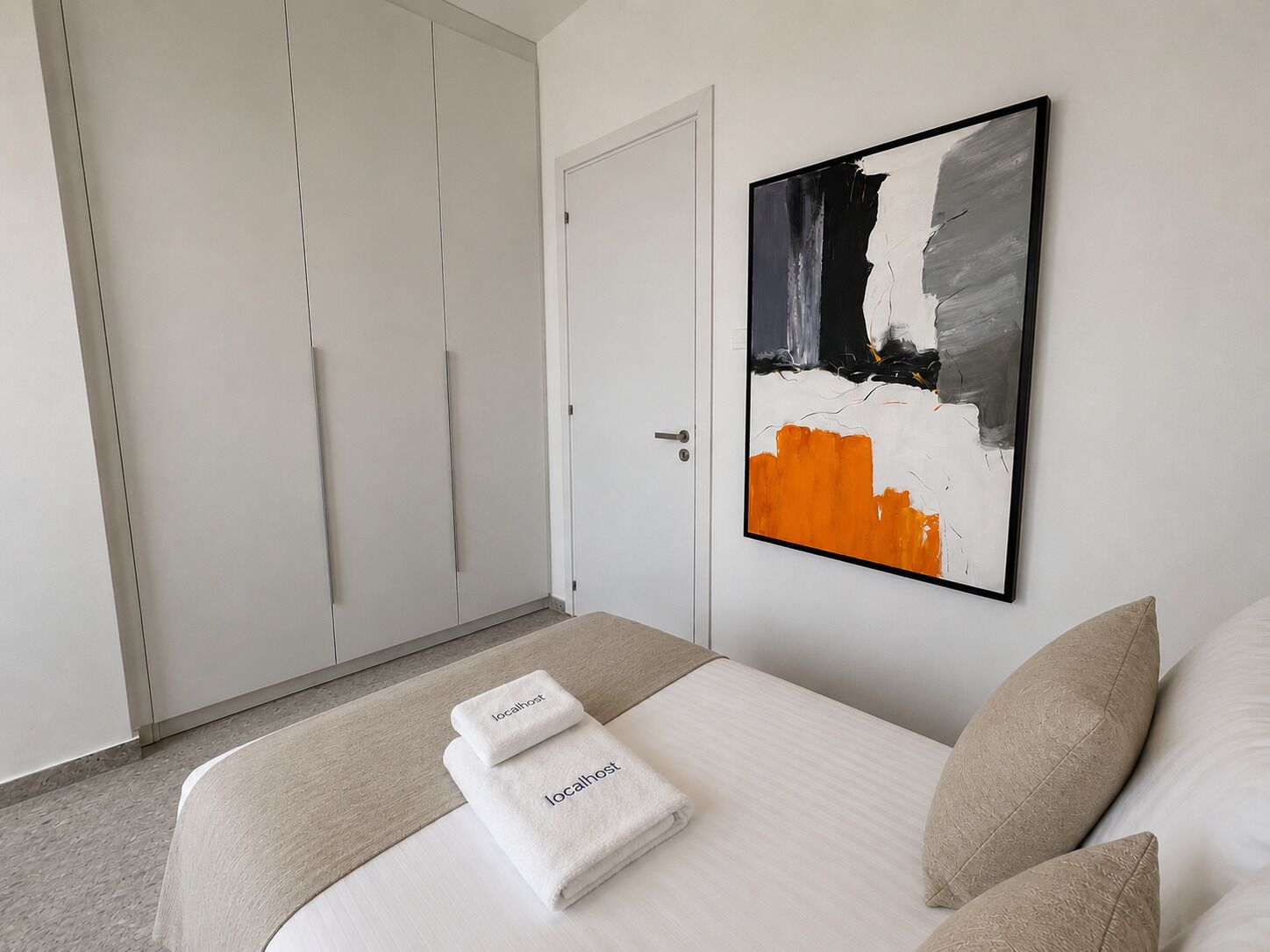 Une chambre d’hôtel avec un lit, une armoire blanche et un tableau au mur.