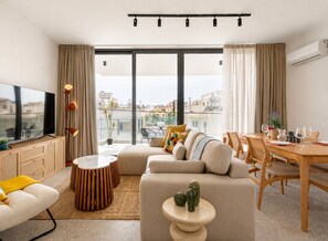 A modern living room with a sofa, a dining table, and a TV. - Solara - Stylish Balcony Apartments in Larnaca (Larnaca)