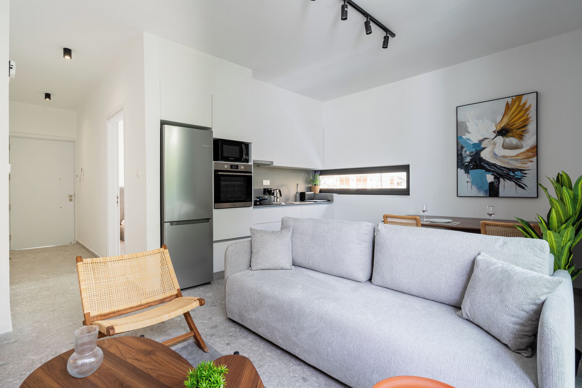 A modern living room with a grey sofa, a wooden coffee table, a wicker chair, and a small plant.