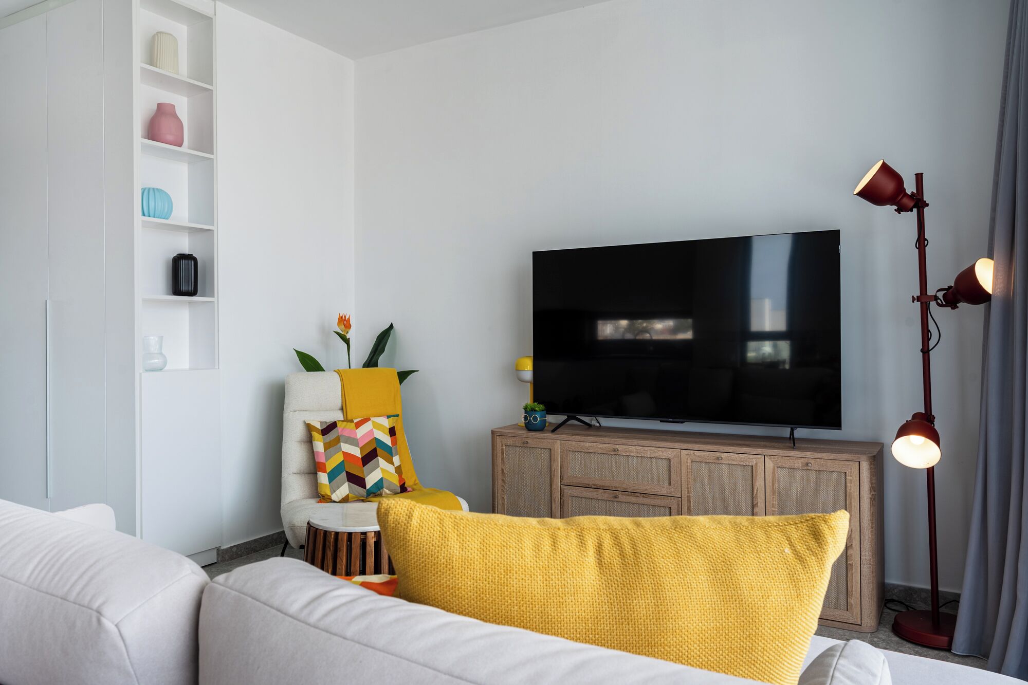 A living room with a flat-screen TV, a sofa, a cabinet, and a floor lamp.