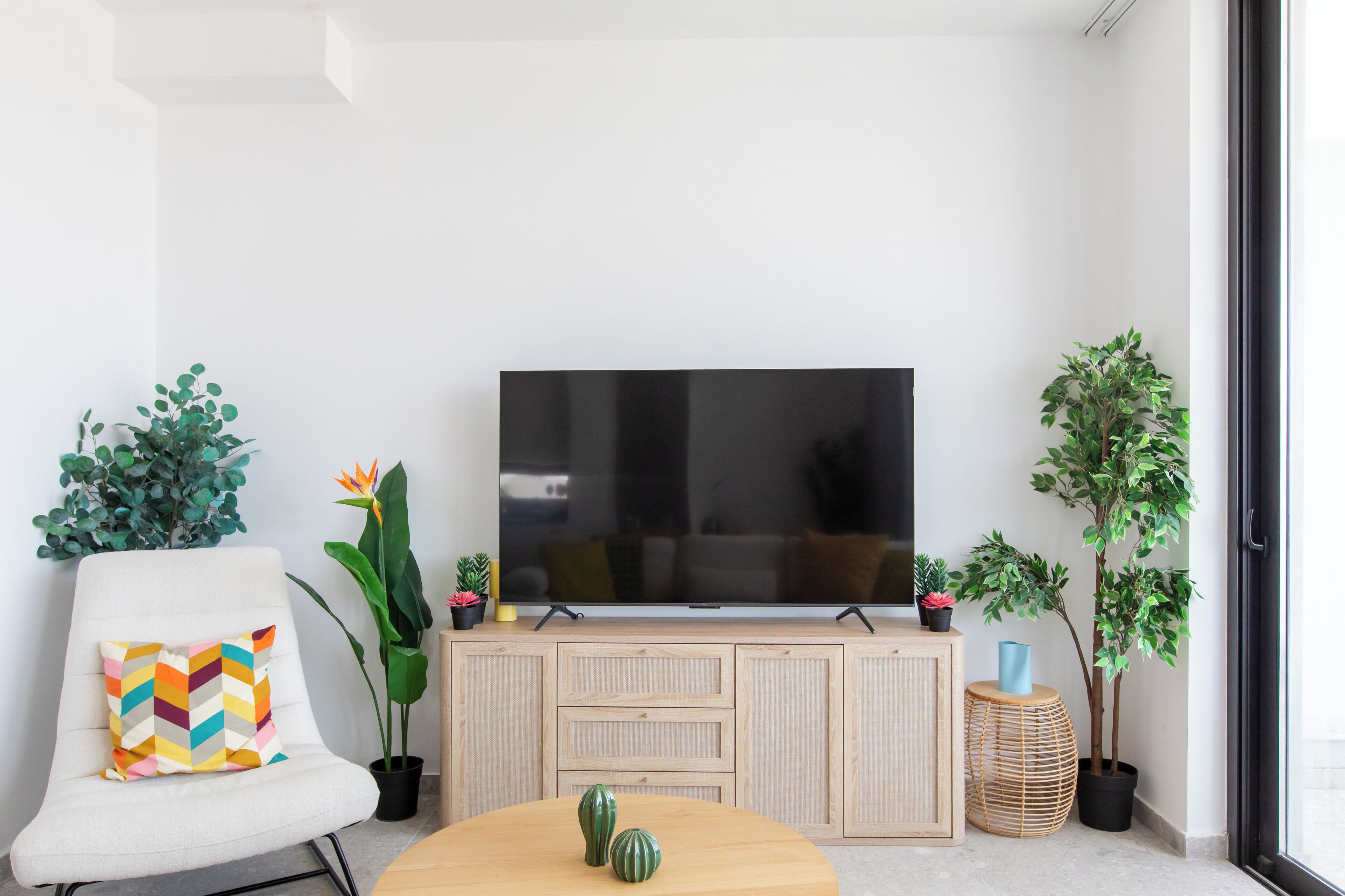 A living room with a TV, a white chair, a round table, and potted plants.