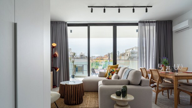 A modern living room with a sofa, coffee table, and dining area. - Solara - Stylish Balcony Apartments in Larnaca (Larnaca)