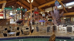Parque acuático interior con piscina, zonas de descanso y una gran escultura arbórea.
