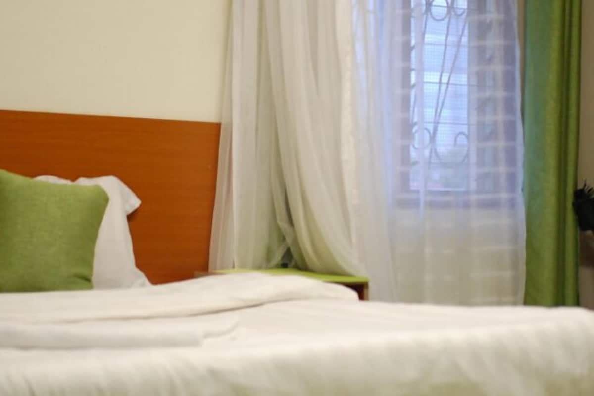 A bed with white bedding, a green pillow, and a wooden headboard.