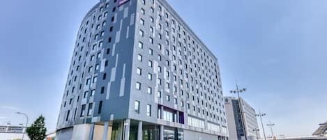 Un hôtel moderne, reconnaissable à son grand panneau Premier Inn, à son entrée en verre et à son parking spacieux où sont stationnées de nombreuses voitures.