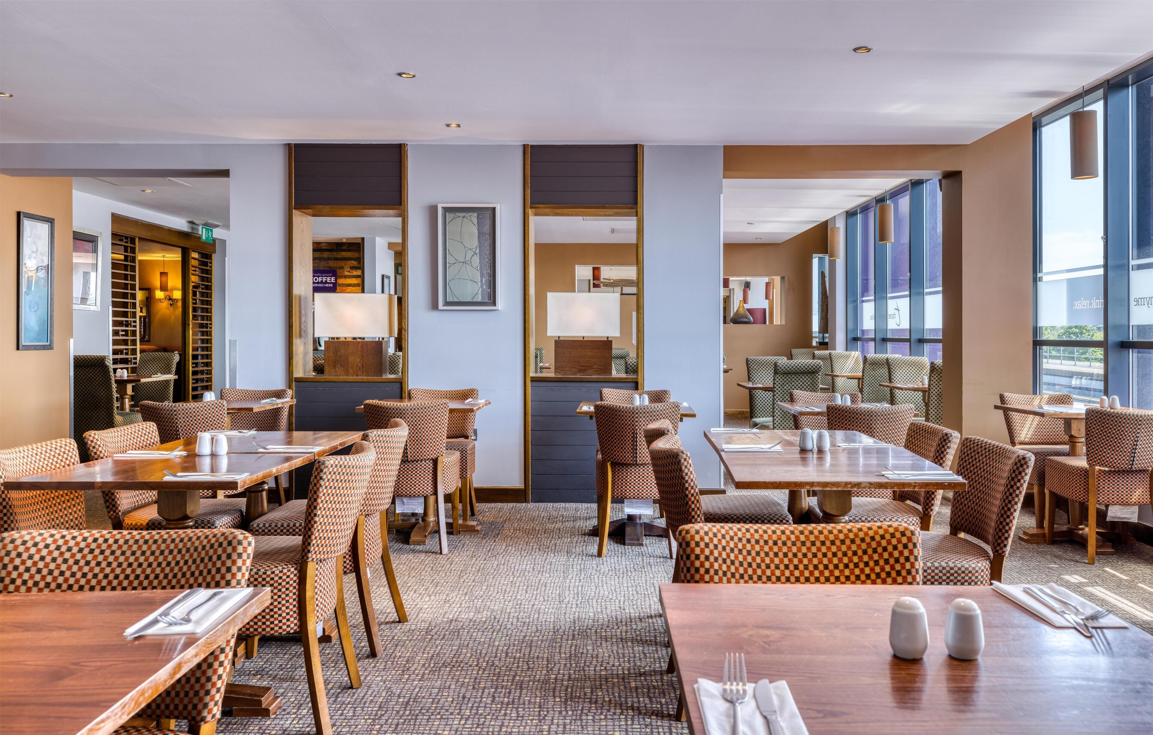 Un espace de restauration d'hôtel avec des chaises à carreaux, des tables en bois et de grandes fenêtres.