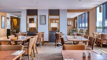 Un espace de restauration d'hôtel avec des chaises à carreaux, des tables en bois et de grandes fenêtres.