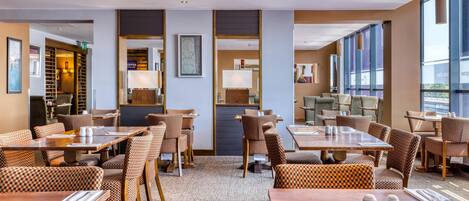 A hotel dining area with checkered chairs, wooden tables, and large windows.