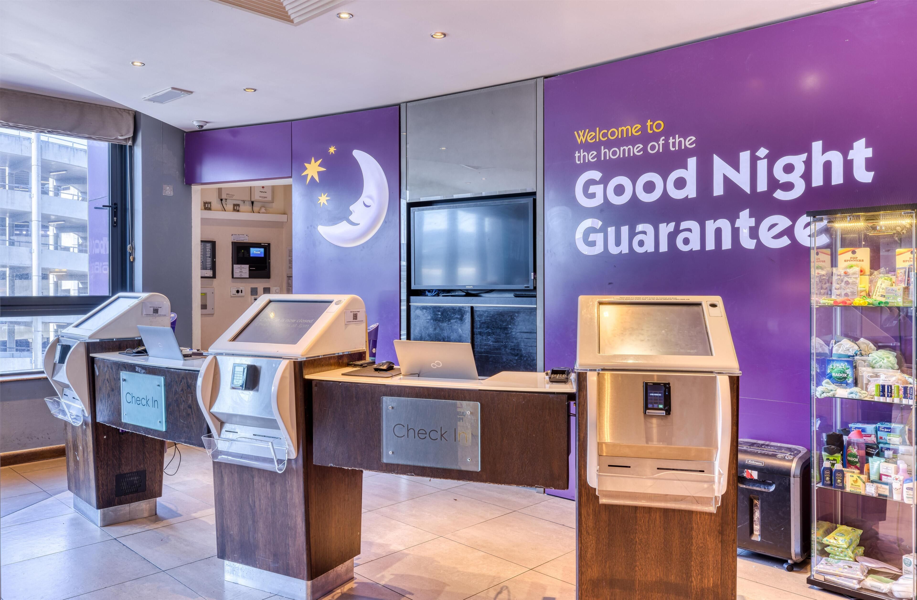 A check-in counter with a 'Check In' sign, a television, and a vending machine with snacks.