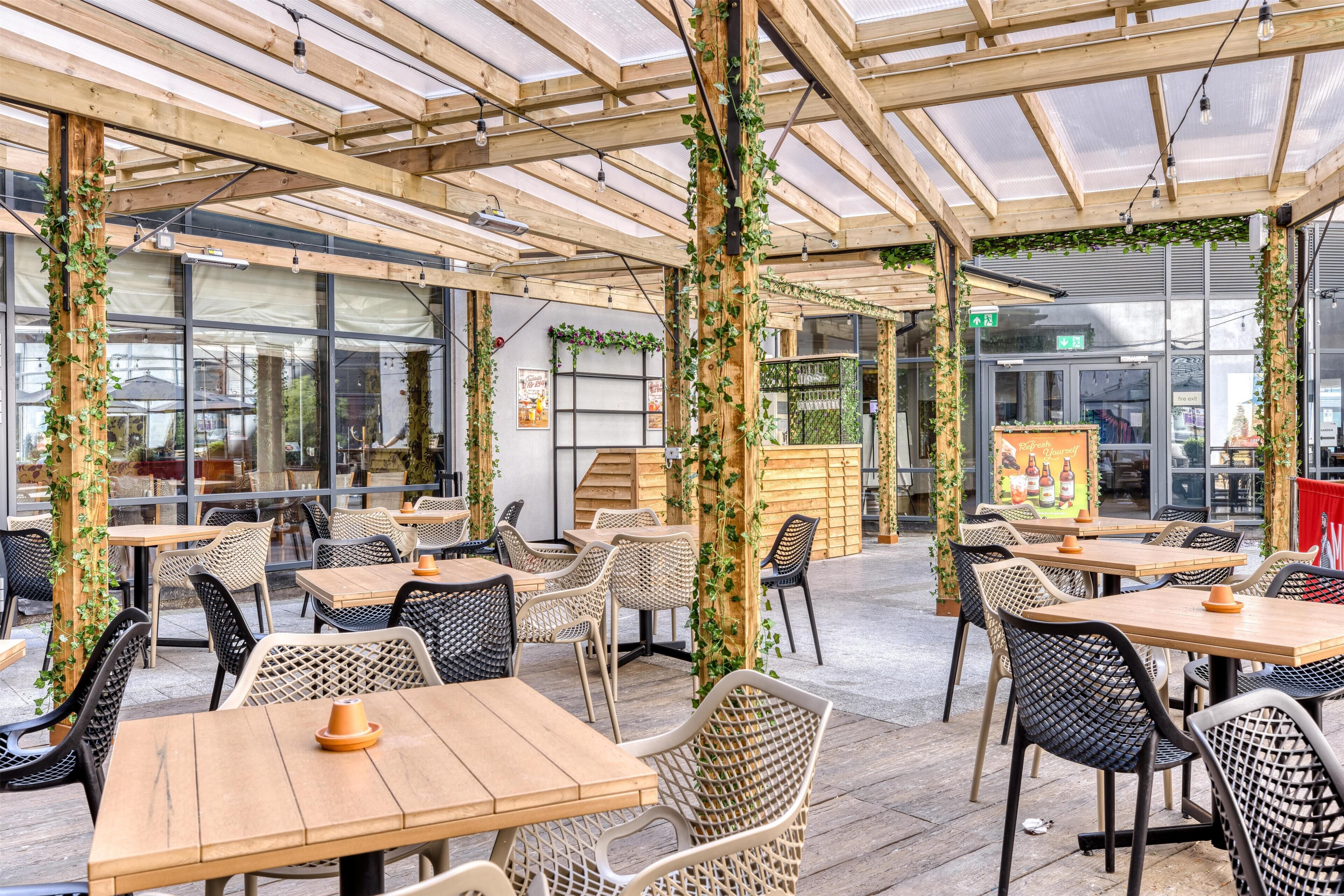 An indoor café with wooden tables and chairs, a glass ceiling, and greenery.