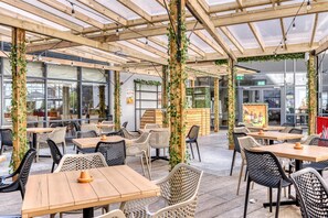 An indoor café with wooden tables and chairs, a glass ceiling, and greenery. - Premier Inn London Gatwick Airport (Gatwick)