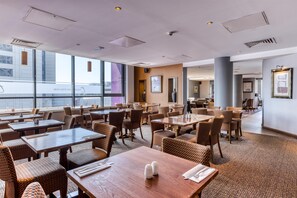 A modern restaurant with high ceilings, large windows, and a mix of wooden and wicker furniture. - Premier Inn London Gatwick Airport (Gatwick)