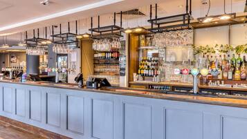 A bar area with a counter, shelves of bottles, and hanging glasses.