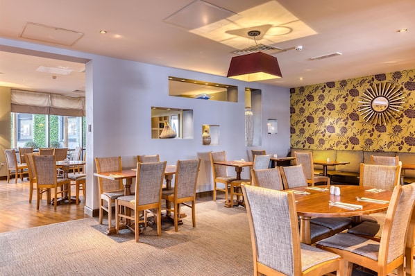 A dining area with wooden tables and chairs, a patterned wall, and a ceiling fan. - Premier Inn London Gatwick Airport (Gatwick)
