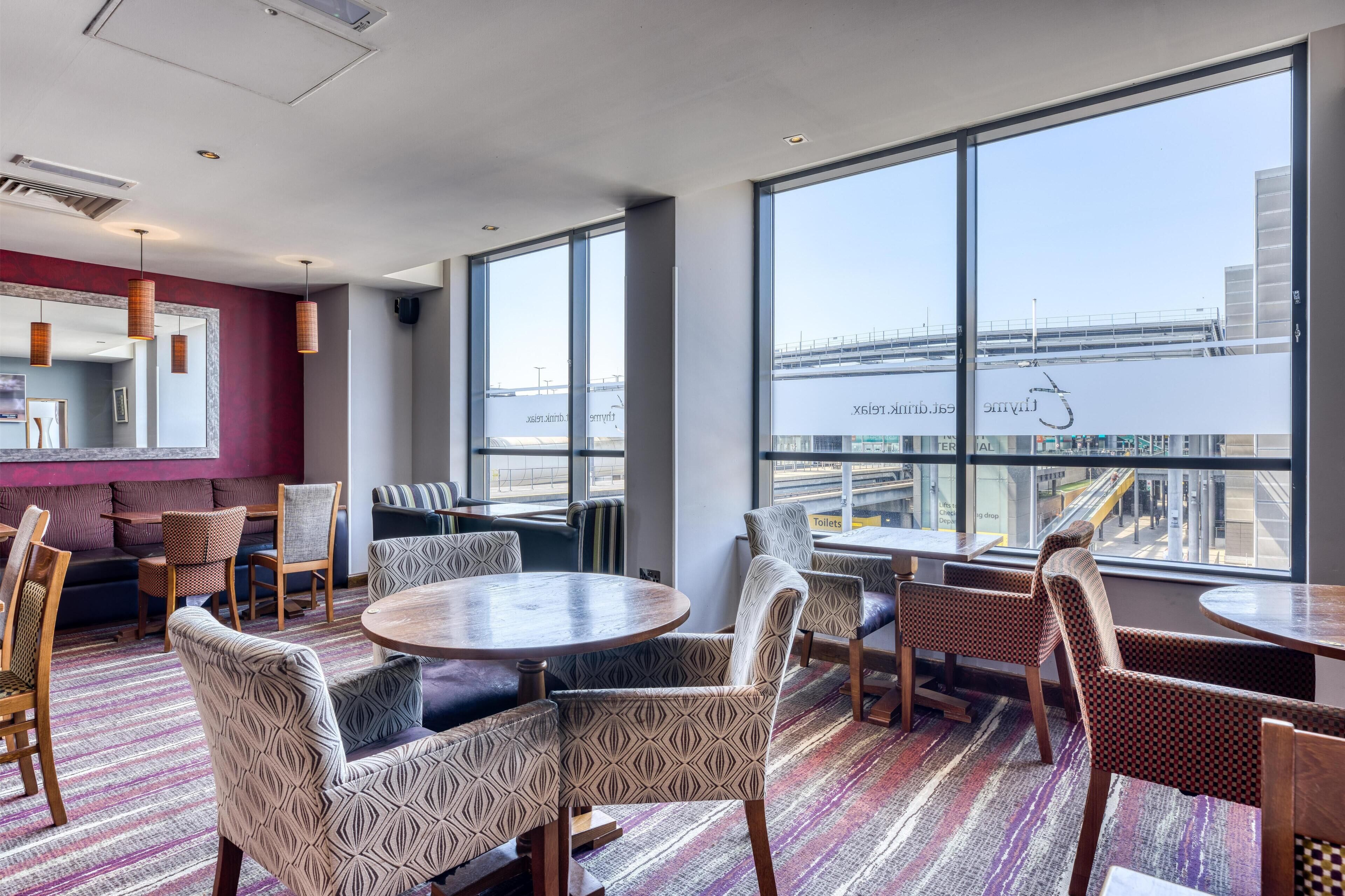 A modern hotel room with large windows, a patterned floor, and a mix of seating options including sofas and chairs.