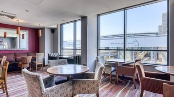 A modern hotel room with large windows, a patterned floor, and a mix of seating options including sofas and chairs.