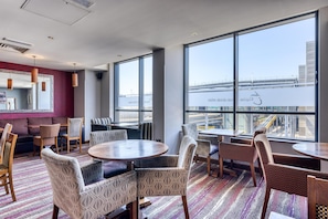 Een moderne hotelkamer met grote ramen, een kamer met een patroon op de vloer, en diverse zitplaatsen, waaronder banken en stoelen.
