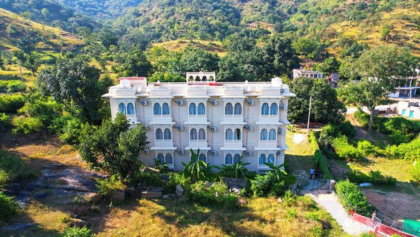 A multi-story building with a traditional architectural style, surrounded by greenery and hills. - Rajkunj Haveli Kumbhalgarh (Kumbhalgarh)