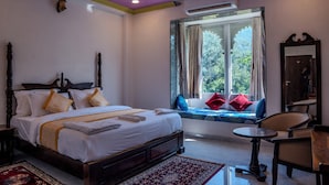 A bedroom with a large bed, a window with a view, a small table, and a chair. - Rajkunj Haveli Kumbhalgarh (Kumbhalgarh)