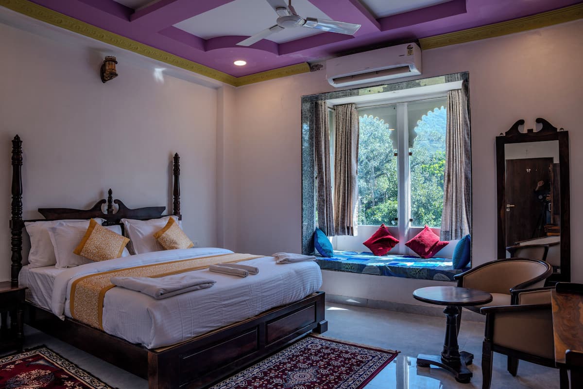 A bedroom with a large bed, a window with a view, a small table, and a chair.