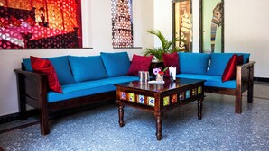 A blue sofa with red cushions, a wooden coffee table with colorful tiles, and a potted plant. - Rajkunj Haveli Kumbhalgarh (Kumbhalgarh)
