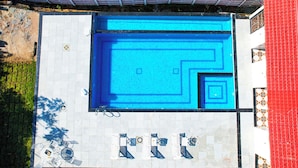 A rooftop swimming pool with a geometric tile design, surrounded by a white tiled deck and a red-roofed building. - Rajkunj Haveli Kumbhalgarh (Kumbhalgarh)