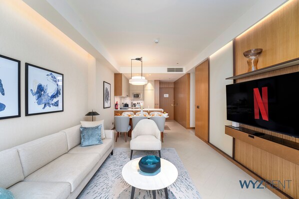 A modern living room with a sofa, a coffee table, a TV, and a dining area in the background.