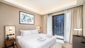 Ein Hotelzimmer mit einem großen Bett, Nachttischlampen, einem Schreibtisch und Blick auf die Stadt durch das Fenster.