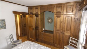 Une chambre à coucher comprenant un lit, une armoire en bois, deux chaises et un miroir décoratif.